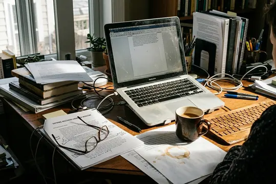 Documentary take on Home office writing setup with laptop, shot mid-afternoon at a cluttered desk